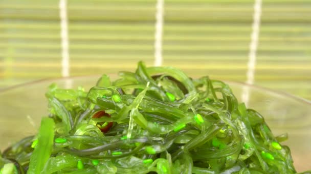 Chuka seaweed is raised with chopsticks by a womans hand.Chuka seaweed in a glass bowl stands — Stock Video