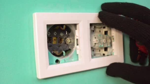 Un electricista con guantes negros instala una toma de corriente. Primer plano - toma de corriente. — Vídeos de Stock