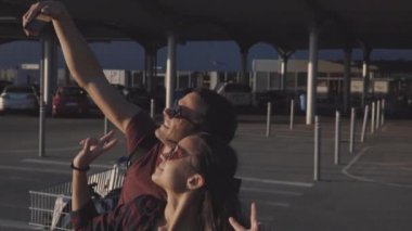 Akşam karanlığında genç bir adam ve bir kız süpermarketin otoparkında kendilerini akıllı bir telefonla filme çekiyorlar..