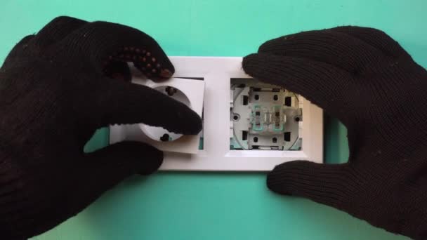 Een elektricien in zwarte handschoenen installeert een stopcontact. Close-up - stopcontact. — Stockvideo