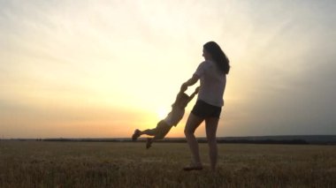 Genç bir anne, doğada gün batımında ellerini tutarak küçük oğlunun etrafında dönüyor..