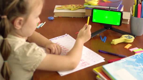 En förskola flicka visar räkna pinnar, tittar in i en smartphone med en grön skärm. Bakifrån. — Stockvideo