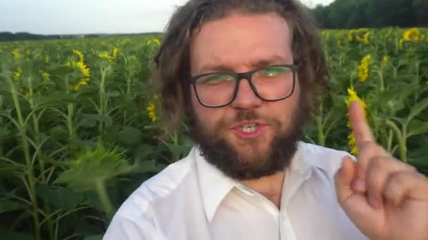 Un joven barbudo está transmitiendo un video de un campo de flores solares.Farmer consulta en línea. — Vídeos de Stock