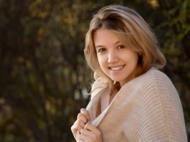 Rengarenk sonbahar ormanlarında neşeli bir şekilde gülümseyen heyecanlı bir düşkün kadın. Güzel, beyaz, genç bir kadın. Sonbahar parkında gülümseyen güzel kız. Güzel, gülümseyen kız sana bakıyor.