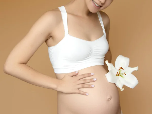 Schöne schwangere junge Frau in Kleidung für Schwangere misst ihren nackten Bauch, lächelnd, auf einem biegen Hintergrund. Bild einer glücklichen Schwangeren, die über einer Mauer posiert. Blick in die Kamera — Stockfoto