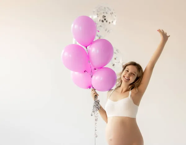 Portret van een mooie gelukkige zwangere vrouw die ballonnen vasthoudt, naar de camera kijkt en glimlacht op een grijze achtergrond. Zwangere vrouw met kleurrijke ballonnen. Schoonheidsmeisje. Het is een jongen.. — Stockfoto