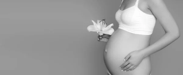 Mooie zwangere jonge vrouw in kleding voor zwangere vrouwen is het meten van haar blote buik, glimlachen, op een biege achtergrond. Foto van een gelukkige zwangere vrouw die over de muur poseert. Kijkend naar camera — Stockfoto
