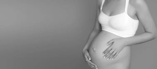 Schöne schwangere junge Frau in Kleidung für Schwangere misst ihren nackten Bauch, lächelnd, auf einem biegen Hintergrund. Bild einer glücklichen Schwangeren, die über einer Mauer posiert. Blick in die Kamera — Stockfoto