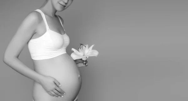 Vacker gravid ung kvinna i kläder för gravida kvinnor mäter hennes nakna mage, leende, på en biege bakgrund. Bild på lycklig gravid kvinna som poserar över muren. Titta på kameran — Stockfoto