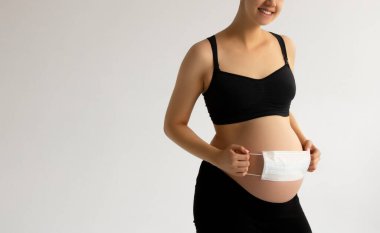 Covid19 koronavirüs ve salgın virüs belirtileri. Karnını ameliyat maskesiyle kapat. Karnındaki bebeği Covid-19 virüsünden veya Coronavirus salgınından korumak için. Çocuk koruması