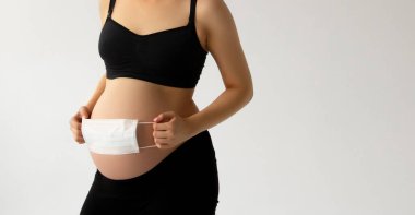 Covid19 koronavirüs ve salgın virüs belirtileri. Karnını ameliyat maskesiyle kapat. Karnındaki bebeği Covid-19 virüsünden veya Coronavirus salgınından korumak için. Çocuk koruması