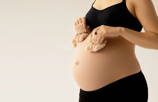 Kleine Schuhe für das Ungeborene im Bauch einer Schwangeren. Aus nächster Nähe. Mutterschaft, Schwangerschaft, Menschen und Erwartungskonzept. Schwangere erwartet Baby. Schönheit Frau mit auf weißem Hintergrund — Stockfoto