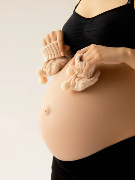 Kleine Schuhe für das Ungeborene im Bauch einer Schwangeren. Aus nächster Nähe. Mutterschaft, Schwangerschaft, Menschen und Erwartungskonzept. Schwangere erwartet Baby. Schönheit Frau mit auf weißem Hintergrund — Stockfoto