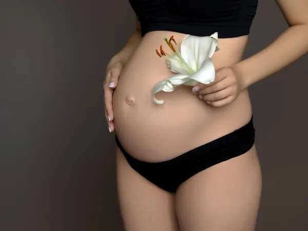 Schöne schwangere junge Frau in Kleidung für Schwangere misst ihren nackten Bauch auf einem grauen Hintergrund. Schwangere misst ihren großen Bauch. Mutterschaft, Schwangerschaft, Menschenbild — Stockfoto