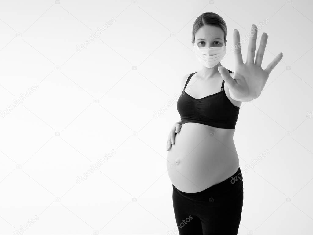 Pregnant woman wearing face mask protective for spreading of disease virus. A pregnant woman wears a surgical mask to protect a COVID-19 show stop sign shape by hand to prevent infection to the fetus