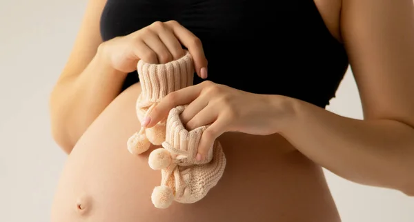 Маленьке взуття для ненародженої дитини в животі вагітної жінки. Близько. Батьківство, вагітність, люди та концепція очікування. Вагітна жінка очікує дитину. Красуня жінка з на білому тлі — стокове фото