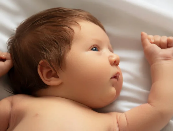 Szép újszülött kisfiú közelkép. Feküdni a fehér ágyban. Aranyos újszülött 1 hónapos, fehér lepedőn pelenkában. Újszülött ellátás, hasfájás, fogak, újszülött nap — Stock Fotó