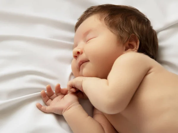 Egy kislány mosolygós arccal alvás közben. A kislány fehér takarón alszik. Gyönyörű portré egy 14 napos, kéthetes kislányról. Anyaság — Stock Fotó