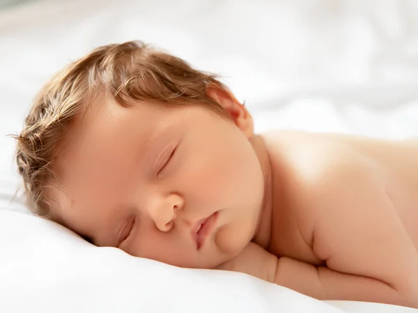 Egy kislány mosolygós arccal alvás közben. A kislány fehér takarón alszik. Gyönyörű portré egy 14 napos, kéthetes kislányról. Anyaság — Stock Fotó