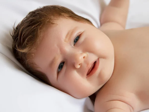 Месячный ребенок лежит и плачет из-за голода на белом матрасе. Младенец чувствует себя нехорошо из-за сонливости. Новорожденный на белом одеяле. Красивый портрет маленькой девочки — стоковое фото