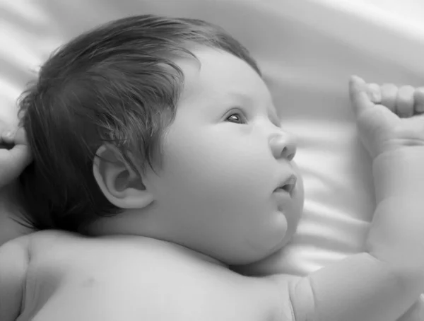 Ładny nowonarodzony chłopiec, portret z bliska. Leży w białym łóżku. Cute noworodka 1 miesiąc życia na białym prześcieradle w pieluszce. Pielęgnacja noworodków, kolka, zęby, noworodek — Zdjęcie stockowe