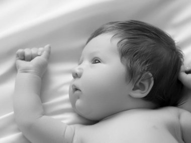 Yeni doğmuş güzel bir erkek bebek portresi. Beyaz yatakta yatıyor. Bebek bezli beyaz çarşafla 1 aylık şirin bir bebek. Yeni doğan bakımı, kolik, dişler, yeni doğan gün