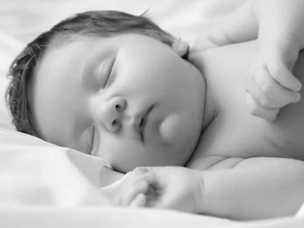 Kleines Mädchen schläft. Neugeborenes Baby in einem Tuch auf weißer Decke. Schönes Porträt des kleinen Mädchens 7 Tage, eine Woche alt. Baby auf dem Rücken liegend auf weißem Hintergrund. Mutterschaft Stockbild