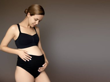 Hamilelik, dinlenme, insanlar ve beklenti konsepti. Mutlu hamile kadın beyaz stüdyoda karnına dokunuyor.