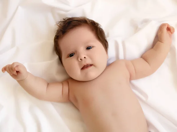 생후 1 개월된 여아가 침대에 누워 머리를 위로 들고 큰 눈으로 카메라를 들여다 봅니다. 침실의 자연 조명. 아기. 건강 과 의학적 개념. 행복 한 임신 출산 — 스톡 사진
