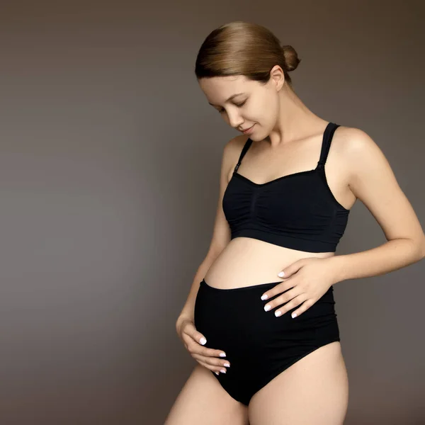 Schwangerschaft, Ruhe, Menschen und Erwartungskonzept - glückliche Schwangere berührt ihren Bauch im weißen Studio — Stockfoto