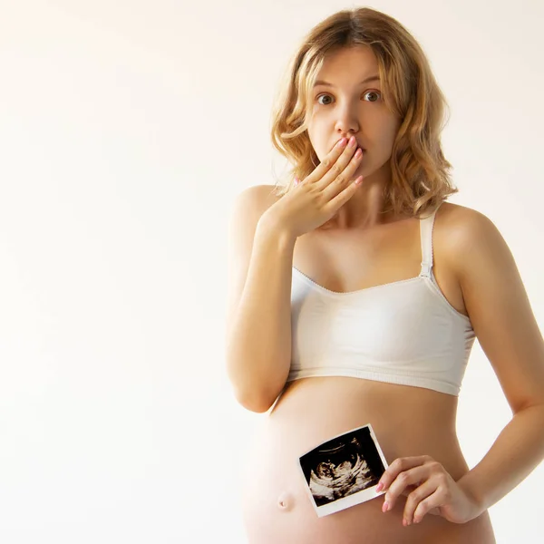 Ecografía prenatal. Belleza sorprendida embarazada sosteniendo imagen de ecografía del bebé nonato dentro de su gran vientre. feliz embarazada mamá mostrando feto usi escanear imagen a cámara Fotos De Stock