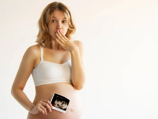 Pränatale Ultraschalluntersuchung. Überraschte schwangere Schönheit mit Sonogramm-Bild des ungeborenen Babys in ihrem großen Bauch. Glückliche werdende Mutter zeigt Fötus usi Scan-Bild vor die Kamera Stockfoto