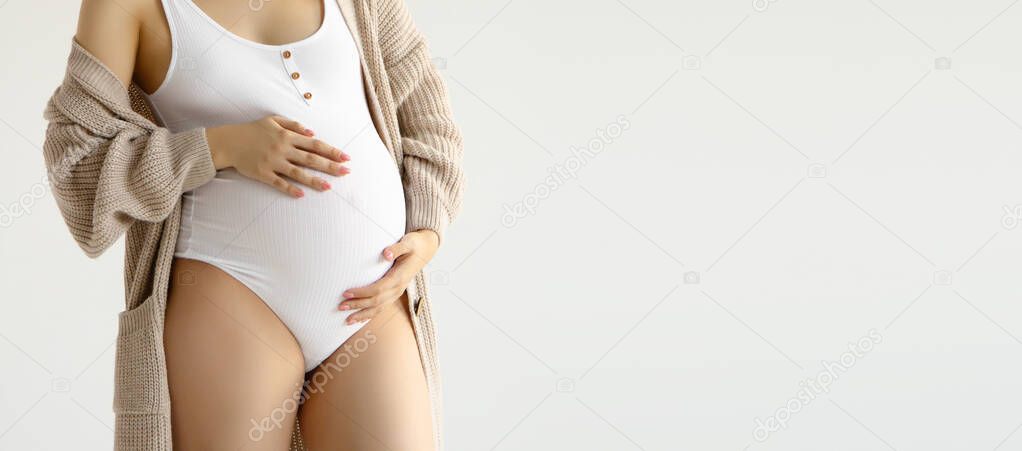 Woman standing and touching with hands her big belly. Isolated on gray background. Emotional loving pregnancy time - 37 weeks. Baby expectation. Love, happiness and safety concept. Closeup