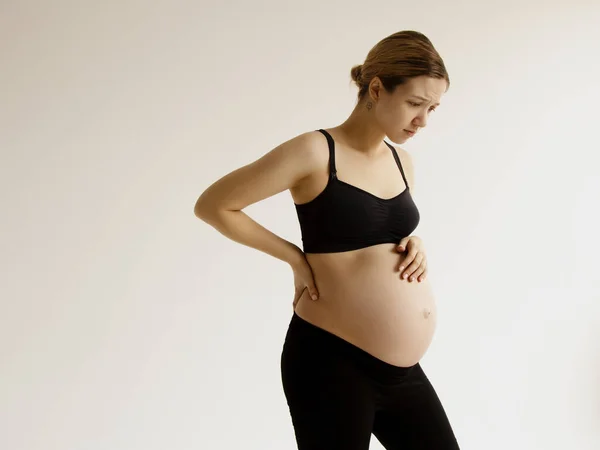 Gravid kvinna med stark smärta masserar sin ryggvärk - smärta i rött. Gravid kvinna med ryggsmärta. Begreppet graviditetshälsa — Stockfoto