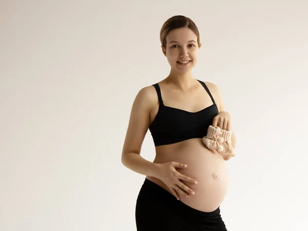 Жінка стоїть і торкається її голий великий живіт. Ізольовані на сірому фоні. Емоційний час люблячої вагітності - 37 тижнів. Дитячі очікування. Концепція любові, щастя та безпеки. крупним планом Стокове Фото
