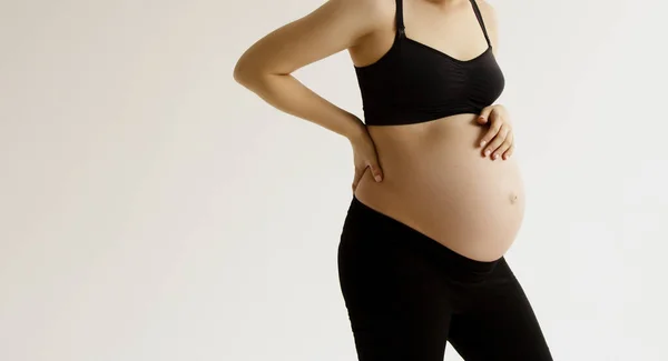 Kvinnan står och rör med händerna sin nakna stora mage. Isolerad på grå bakgrund. Känslomässig kärleksfull graviditetstid - 37 veckor. Förväntad bebis. Kärlek, lycka och säkerhet koncept. Närbild — Stockfoto