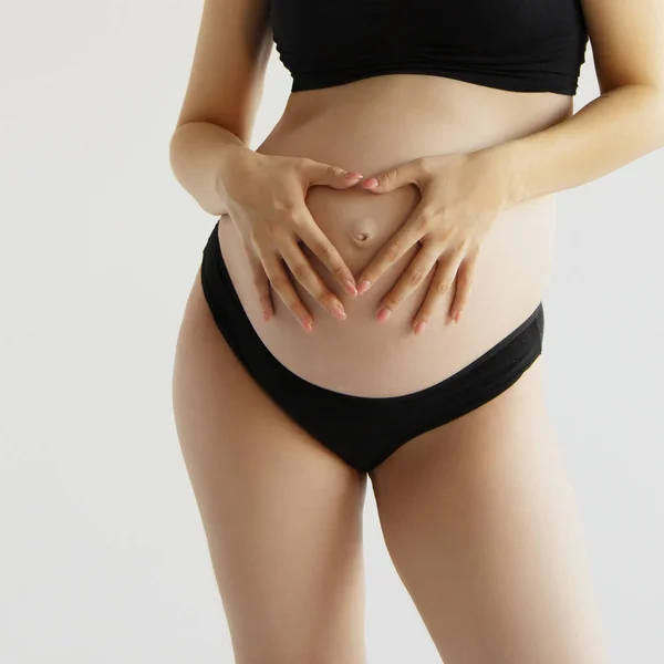 Mujer de pie y tocando con las manos su gran barriga desnuda. Aislado sobre fondo gris. El tiempo de embarazo emocional cariñoso - 37 semanas. Esperanza del bebé. Amor, felicidad y concepto de seguridad. Primer plano. Imágenes De Stock Sin Royalties Gratis