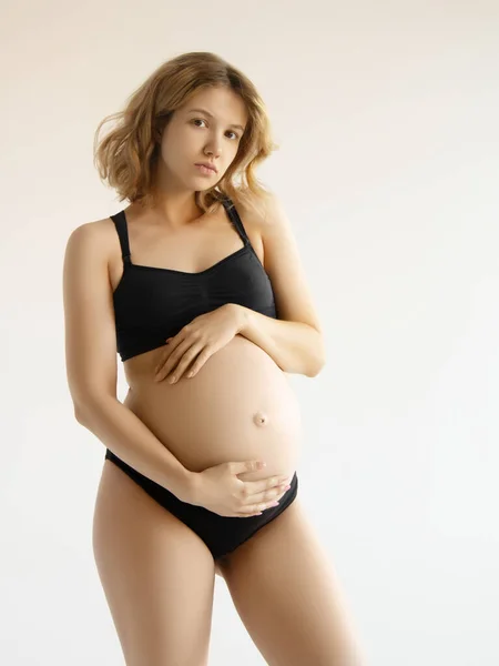 Frau, die steht und mit den Händen ihren nackten dicken Bauch berührt. Vereinzelt auf grauem Hintergrund. Emotional liebevolle Schwangerschaftszeit - 37 Wochen. Babyerwartung. Liebe, Glück und Sicherheitskonzept. Nahaufnahme — Stockfoto