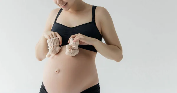 Schwangere Frau hält Babytuch für Neugeborenes isoliert auf weißem Hintergrund.Schwangere Frau packt Babysachen bereit für das Entbindungskrankenhaus.Schwangerschaft Vorbereitung für Neugeborenenkonzept lizenzfreie Stockfotos
