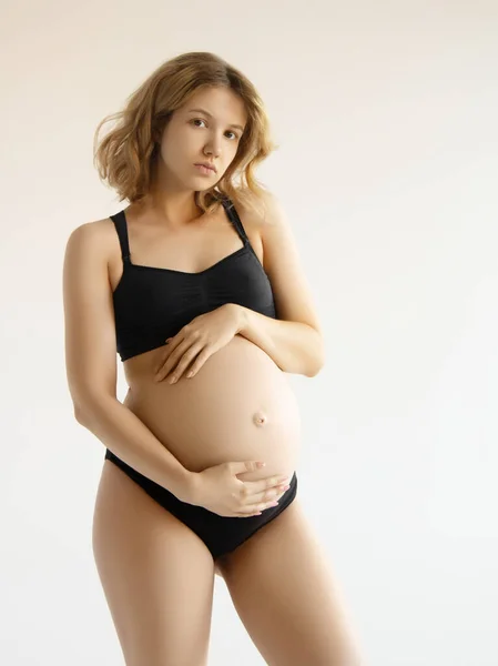Жінка стоїть і торкається її голий великий живіт. Ізольовані на сірому фоні. Емоційний час люблячої вагітності - 37 тижнів. Дитячі очікування. Концепція любові, щастя та безпеки. крупним планом Стокове Фото