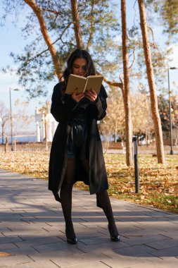 Siyah paltolu bir kızın fotoğrafı. Parkta duruyor ve 