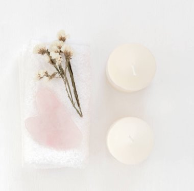 Gua Sha masaj aleti beyaz havludaki gül kuvarstan yapılmış. Mumlar ve kurumuş çiçekler..