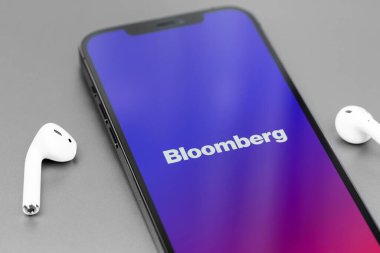 Bloomberg mobile logo app on screen smartphone iPhone with AirPods closeup. Bloomberg L.P. is a privately held financial software, data and media company. Moscow, Russia - July 20, 2021
