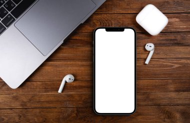 mockup smartphone iPhone 12 Pro Max with blank white screen, AirPods, Macbook on wood background top view Apple is a multinational technology company. Moscow, Russia - June 20, 2021