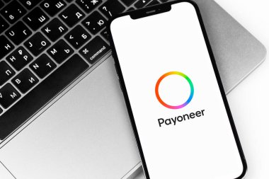 Payoneer logo mobile app on screen smartphone iPhone and MacBook keyboard closeup. Payoneer - payment system. Moscow, Russia -  July 27, 2021
