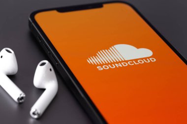 Soundcloud logo mobile app on screen smartphone iPhone and AirPods headphones macro closeup. SoundCloud is a global online audio distribution platform. Moscow, Russia - June 10, 2021