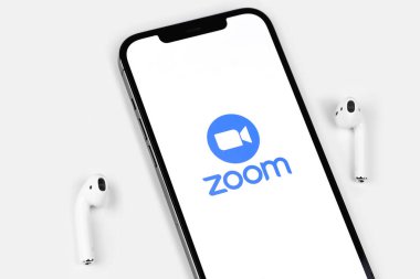 Zoom mobile logo app on screen smartphone iPhone with AirPods on white background. Zoom Video Communications is a company that provides remote conferencing services. Moscow, Russia - June 12, 2021