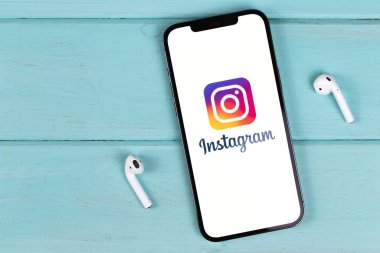 Instagram logo mobile app on screen smartphone iPhone with AirPods on a colored background. Instagram is a photo-sharing app for smartphones. Moscow, Russia - September 26, 2021