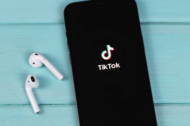 TikTok logo mobile app on screen smartphone iPhone closeup with AirPods on a colored background. TikTok is app to create and share videos. Moscow, Russia -  September 26, 2021