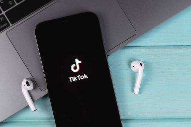 TikTok logo mobile app on screen smartphone iPhone closeup with MacBook and AirPods on a colored background. TikTok is app to create and share videos. Moscow, Russia -  September 26, 2021